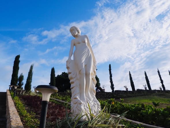 A goddess statue standing at the head of the cypress-lined garden