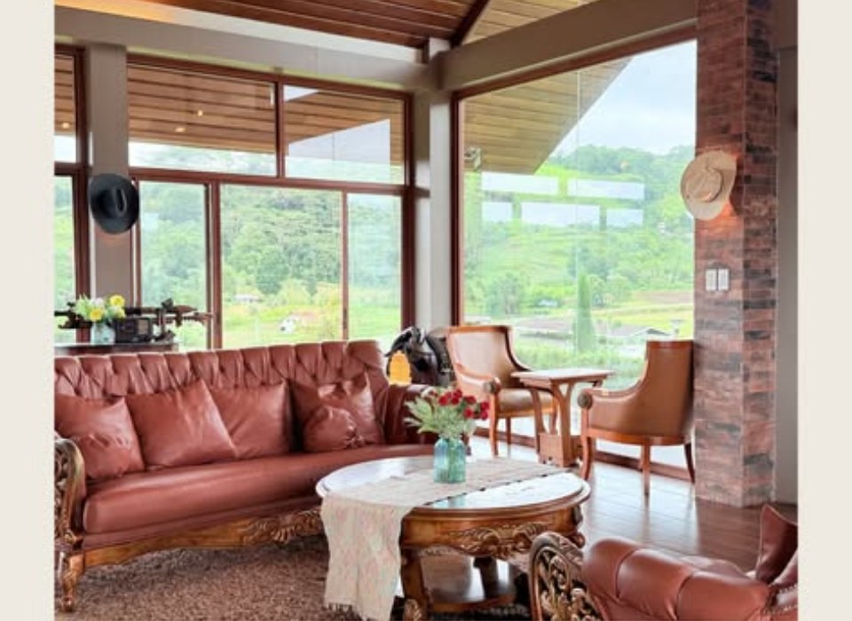 Living room with carved wooden furniture, leather sofas and a view out to the paddocks